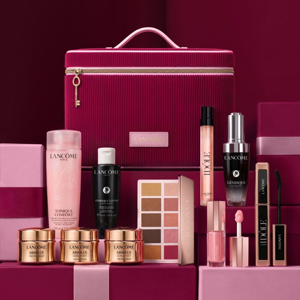 A festive still life showcasing premium Lancome skincare, makeup, and Idole perfume arranged around a cherry-red vanity case.