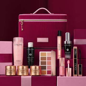 A festive still life showcasing premium Lancome skincare, makeup, and Idole perfume arranged around a cherry-red vanity case.